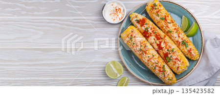 Elotes mexican street corn cob covered in spices and cheese being served on plate Elotes mexican street corn cob covered in spices and cheese being served on plate 135423582