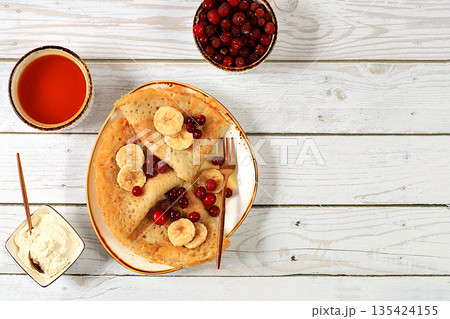 Delicious Russian pancakes with jam, soft cottage cheese, bananas, cranberries, and honey on a marble table. Healthy breakfast made from natural ingredients, Maslenitsa concept, natural products Delicious Russian pancakes with jam, soft cottage cheese, bananas, cranberries, and honey on a marble table. Healthy breakfast made from natural ingredients, Maslenitsa concept, natural products 135424155