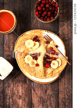 Delicious Russian pancakes with jam, soft cottage cheese, bananas, cranberries, and honey on a marble table. Healthy breakfast made from natural ingredients, Maslenitsa concept, natural products 135424156