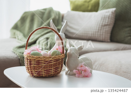 Easter Basket with Ester Eggs,  Plush Bunny and Spring Decor on White Table intoCozy Living Room 135424487