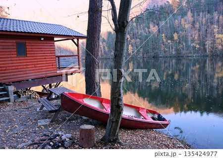 A red canoe is sitting on the shore of a lake next to a wooden cabin A red canoe is sitting on the shore of a lake next to a wooden cabin 135424977