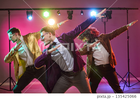 Three stylish male dancers performing disco moves under colorful party lights 135425066