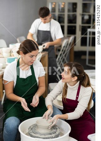 Woman working with pottery wheel and master giving instructions Woman working with pottery wheel and master giving instructions 135425292