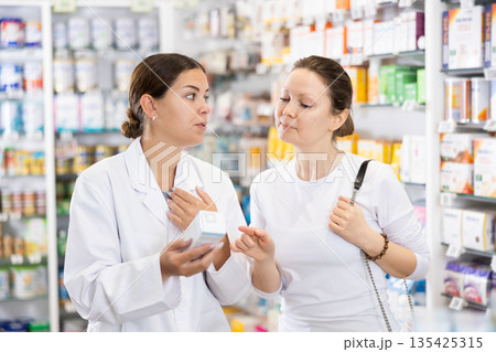 Woman pharmacist helping woman customer to choose remedy in pharmacy Woman pharmacist helping woman customer to choose remedy in pharmacy 135425315