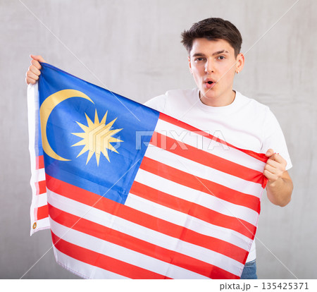 Male fan holds canvas of national Malaysian flag in hands raised above head and chants slogan Male fan holds canvas of national Malaysian flag in hands raised above head and chants slogan 135425371