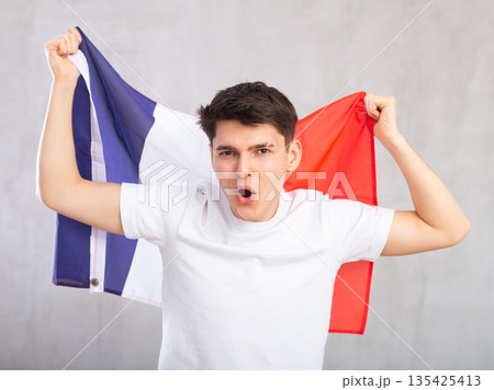 Energized,active male spectator holds national flag of France in hands and chants popular slogan 135425413