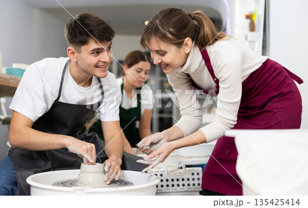 Man working with pottery wheel and master giving instructions 135425414
