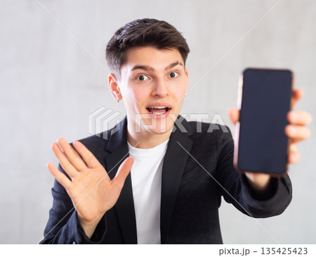 Surprised young guy holding mobile phone in his hand Surprised young guy holding mobile phone in his hand 135425423