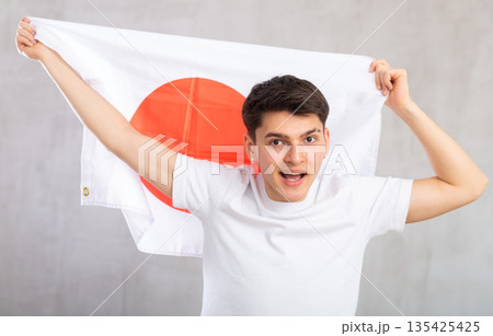 Energized, active male spectator holds national flag of Japan in hands and chants popular slogan. 135425425