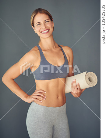 Happy woman, fitness and yoga mat for exercise, zen workout or healthy body against a grey studio background. Portrait of female person yogi with smile and mat for spiritual wellness or mental health Happy woman, fitness and yoga mat for exercise, zen workout or healthy body against a grey studio background. Portrait of female person yogi with smile and mat for spiritual wellness or mental health 135425535