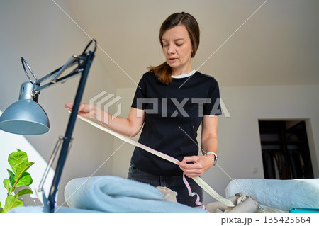 Woman standing indoors measuring fabric with tape measure Woman standing indoors measuring fabric with tape measure 135425664