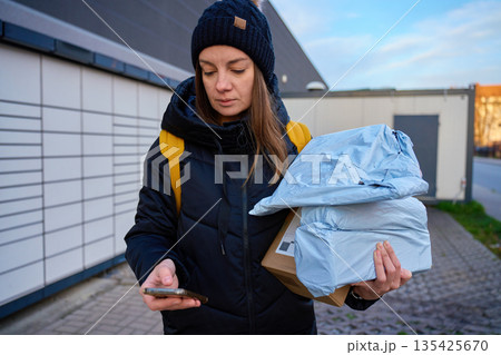 Woman holding multiple parcels and using smartphone near automated parcel lockers Woman holding multiple parcels and using smartphone near automated parcel lockers 135425670