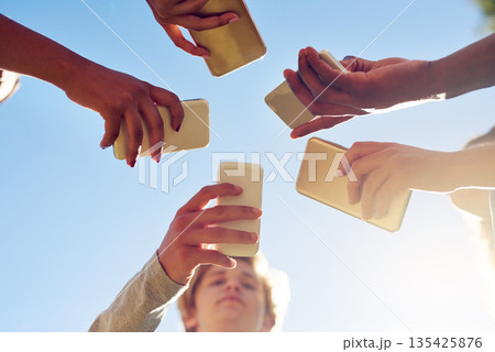 Hands, below and phone by friends together for social media, networking and sharing app on blue sky background. Low angle, smartphone and gen z people with internet, addiction or online communication Hands, below and phone by friends together for social media, networking and sharing app on blue sky background. Low angle, smartphone and gen z people with internet, addiction or online communication 135425876