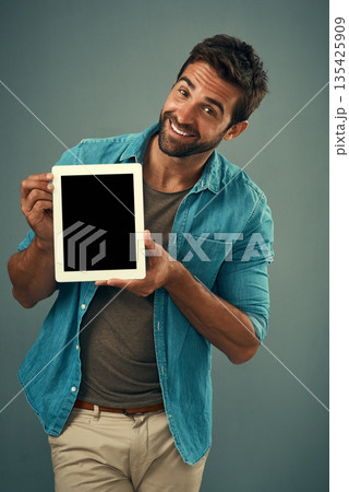 Happy man, tablet and mockup screen for advertising, marketing or branding against a grey studio background. Portrait of male person showing technology display or mock up space for advertisement 135425909