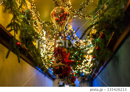 Ceiling decorated with pine branches, colorful lights, red and gold baubles, glittery reindeer, and festive balloon ornament. Ceiling decorated with pine branches, colorful lights, red and gold baubles, glittery reindeer, and festive balloon ornament. 135426213
