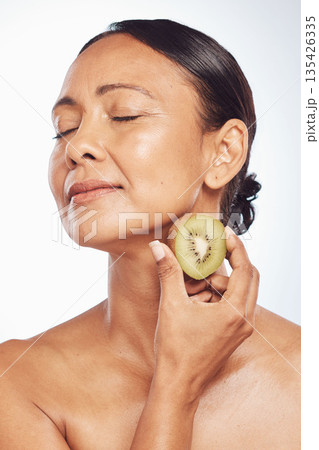 Relax, beauty or mature woman with kiwi for healthy detox, skincare or facial treatment routine in studio. Spa, face or senior model with wellness, self love or fruit isolated on white background Relax, beauty or mature woman with kiwi for healthy detox, skincare or facial treatment routine in studio. Spa, face or senior model with wellness, self love or fruit isolated on white background 135426335
