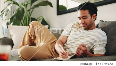 Man, journal and writing on sofa in home, daily reflection or idea notes to relax for creativity. Person, notebook for planning or sketching with agenda in diary, to do list or goal setting at house Man, journal and writing on sofa in home, daily reflection or idea notes to relax for creativity. Person, notebook for planning or sketching with agenda in diary, to do list or goal setting at house 135426528