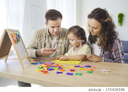 Parents teaching daughter alphabet with magnetic letters in a cozy home setting Parents teaching daughter alphabet with magnetic letters in a cozy home setting 135426596