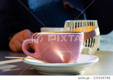 Two coffee cups with a heart latte art cappuccino on a cafe table on a sunny day with a person sitting in the background. Selective focus Two coffee cups with a heart latte art cappuccino on a cafe table on a sunny day with a person sitting in the background. Selective focus 135426798