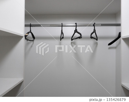 Empty white closet interior with black hangers on a metal rod. Wardrobe storage background with copy space 135426879