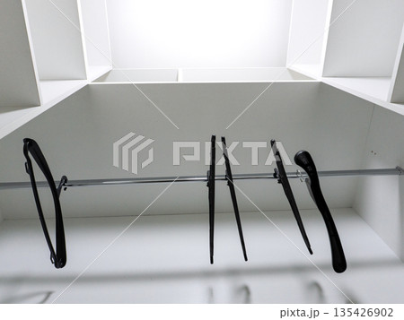 Low angle view of black hangers in an empty white closet. Interior wardrobe storage with shelves and metal rod. Minimalist home organization concept 135426902