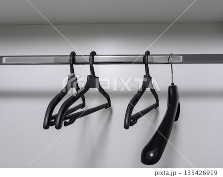 Three black clothes hangers hanging on a metal rod in an empty white closet. Wardrobe storage and organization concept with copy space 135426919