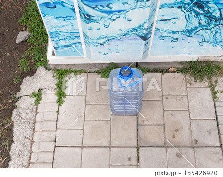 Large plastic water bottle on tiled pavement near vending kiosk. Filled clear container with blue handle outdoors. Clean drinking water supply 135426920