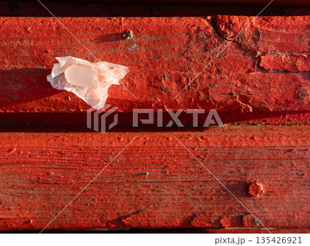 Unwrapped white hard candy on a crumpled wrapper placed on red painted wood. Weathered wooden texture with peeling paint and strong sunlight shadow 135426921