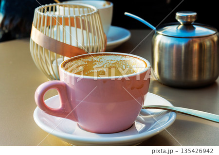 Empty pink coffee cup with latte residue on saucer with spoon  and blurred decor behind on sunlit cafe table 135426942