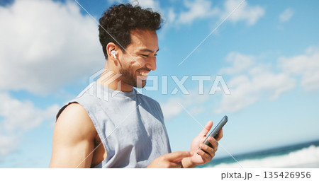 Beach, below and happy man with fitness, smartphone and online reading for text message. Ocean, cellphone and person with smile, social media and digital app to track progress, internet and exercise 135426956
