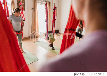 Women learning aerial vinyasa yoga class with hammocks Women learning aerial vinyasa yoga class with hammocks 135427054