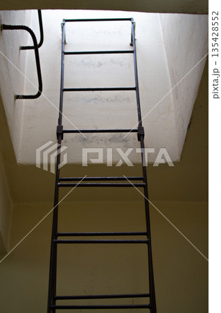 View of a metal ladder leading to a small, illuminated opening above 135428552