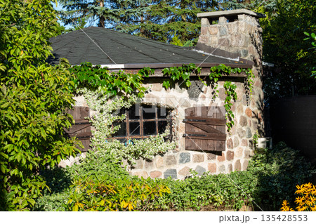 Charming stone cottage surrounded by lush greenery in a serene garden setting 135428553