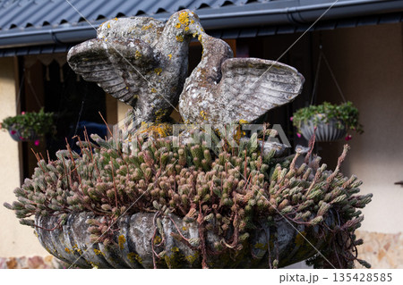 Stone fountain with bird sculptures and blooming greenery in a peaceful Stone fountain with bird sculptures and blooming greenery in a peaceful 135428585