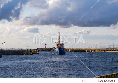 Coastal vessel navigating through a harbor entrance under a cloudy sky Coastal vessel navigating through a harbor entrance under a cloudy sky 135428594
