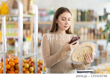 In shop young woman scans QR code and take reading on cheese pizza package using phone camera In shop young woman scans QR code and take reading on cheese pizza package using phone camera 135428746