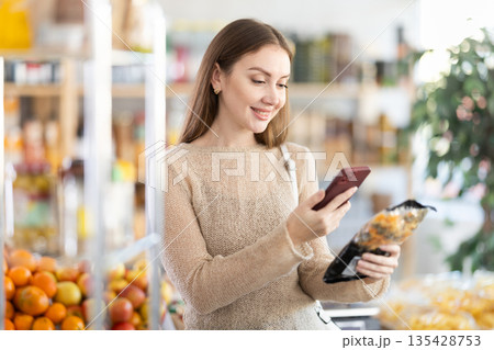 Female buyer checks suitability - scans QR code on pasta label in grocery store 135428753