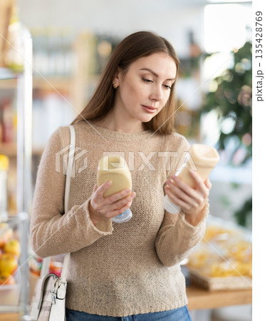 Young woman choosing mayonnaise in grocery store Young woman choosing mayonnaise in grocery store 135428769