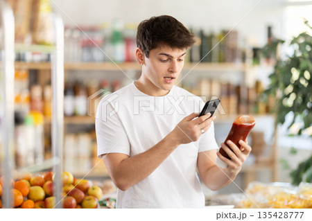 In shop young man scans QR code and take reading on ketchup package using phone camera 135428777