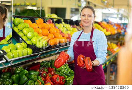 Positive middle-aged woman market assistant arranging organic bell pepper in grocery shop Positive middle-aged woman market assistant arranging organic bell pepper in grocery shop 135428860