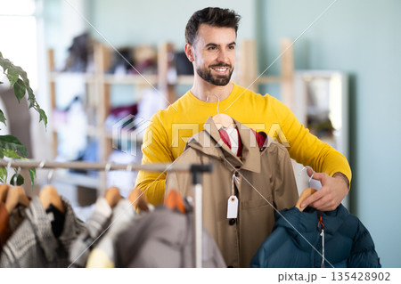 Young man choosing down jacket in clothing store Young man choosing down jacket in clothing store 135428902