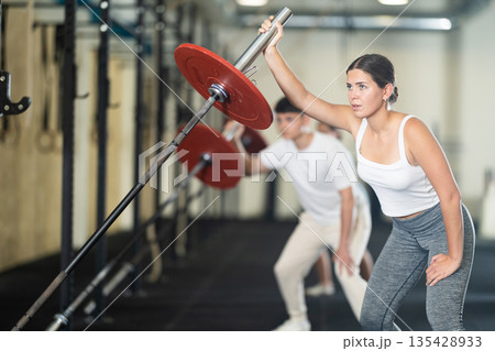 Young woman training with barbell with one arm 135428933