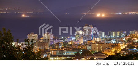 Harbour, buildings and city at night with lights, urban development and streets. Dark, travel and outdoor residential architecture of downtown with ocean or sea water in the evening with a skyline. 135429113
