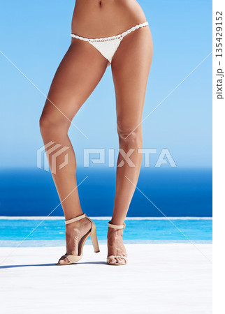 Legs, woman and bikini body closeup with heels at beach, ocean and waves or tan, skin and high shoes. Summer fashion, beauty or travel and pool, sea and spa or female model, wellness and blue sky 135429152