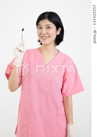 歯科用の器具を持って微笑むスクラブを着た女性 歯科用の器具を持って微笑むスクラブを着た女性 135429357