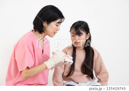 模型を使って子供の患者に歯磨き指導をする歯科衛生士 135429743