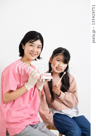 カメラ目線で微笑む歯科衛生士と小学生の女の子 カメラ目線で微笑む歯科衛生士と小学生の女の子 135429751