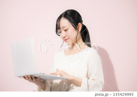 ピンクの背景でパソコンを持つタイピングする若い女性 ピンクの背景でパソコンを持つタイピングする若い女性 135429995