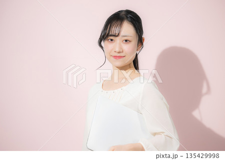 ピンクの背景でパソコンを持つ若い女性 ピンクの背景でパソコンを持つ若い女性 135429998
