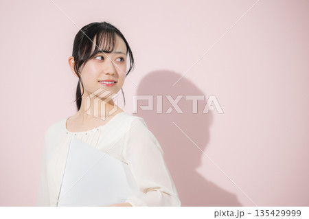 ピンクの背景でパソコンを持つ若い女性 振り返る ピンクの背景でパソコンを持つ若い女性 振り返る 135429999